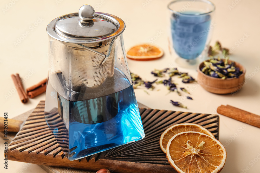 Teapot of tasty blue tea and dried fruits on color background, closeup