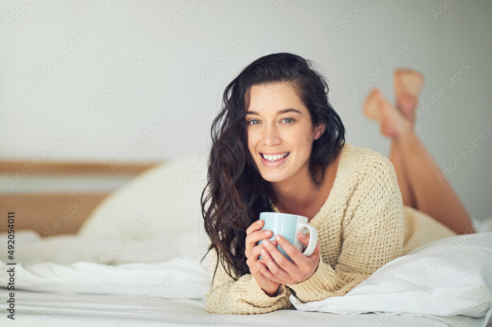 Easing my way into the weekend. Full length portrait of a young woman drinking coffee while lying on