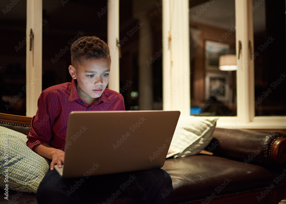 Too much tech too late. Shot of a young boy using a laptop past his bedtime at home.