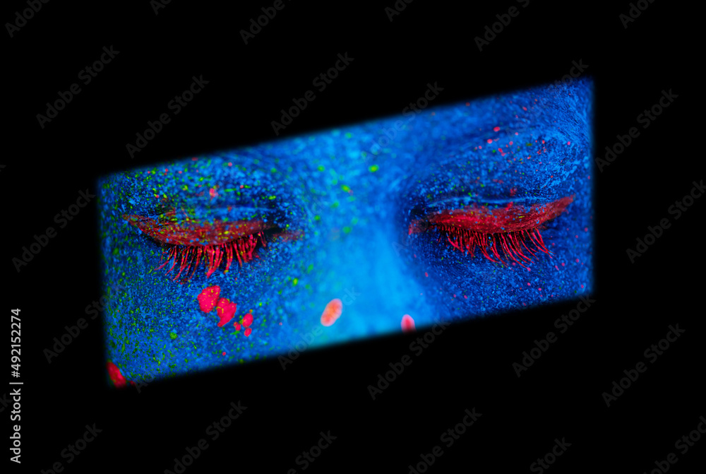 Shes a mystery. Shot of a young woman posing with neon paint on her face.