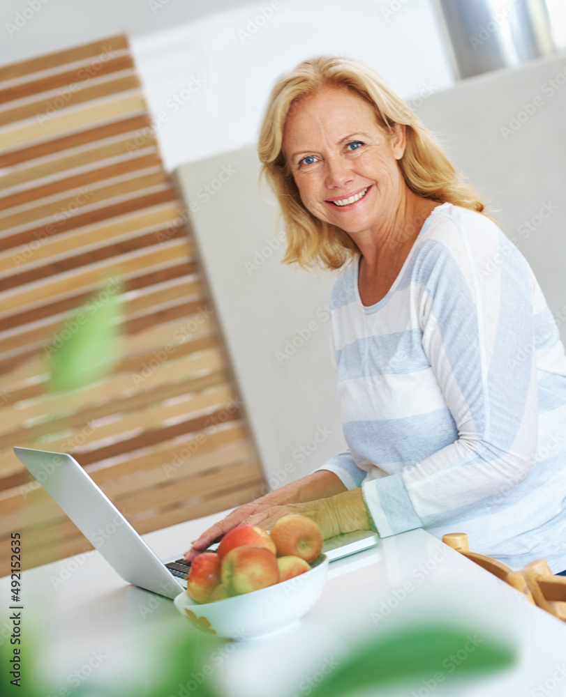 Theres no time for boredom. Portrait of a senior woman sitting in her kitchen using a laptop.