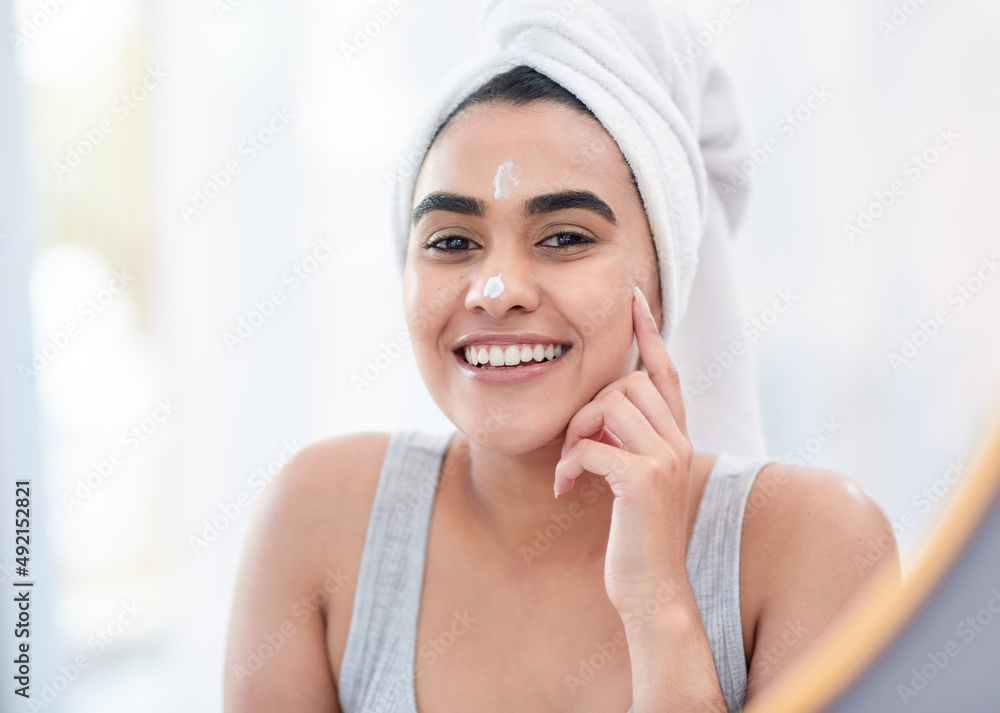 Start your day the fresh way. Shot of happy young woman applying facial moisturiser in front of her 