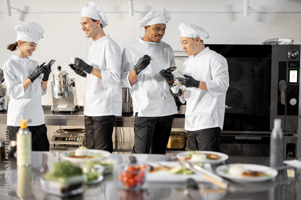 Team of multiracial cooks having conversation during a coffee break in the kitchen. Well-dressed che