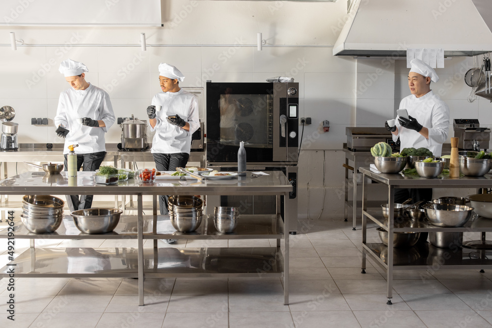 Group of cooks using phones and drinking coffee during a break in the restaurant kitchen. Profession