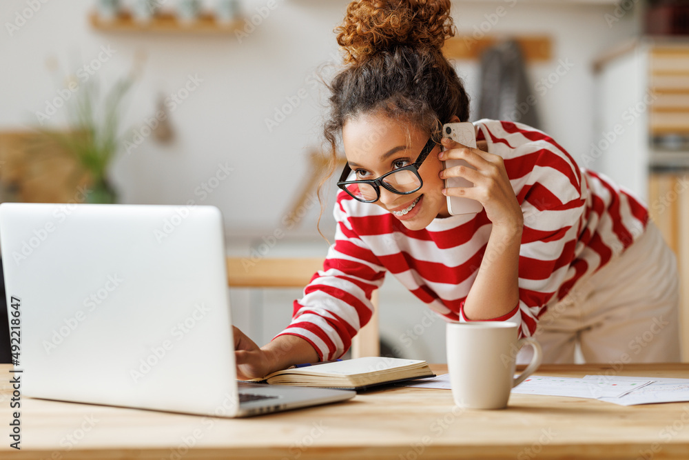 Smiling  african american self-employed woman talking on phone while working remotely on laptop