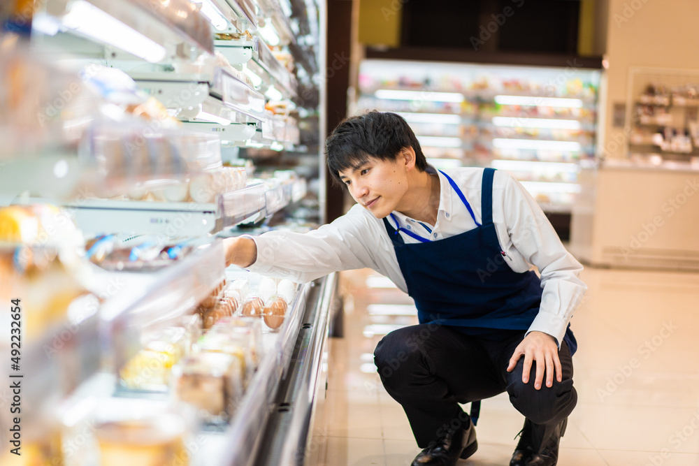 食品スーパーで品出しをする若いスタッフ