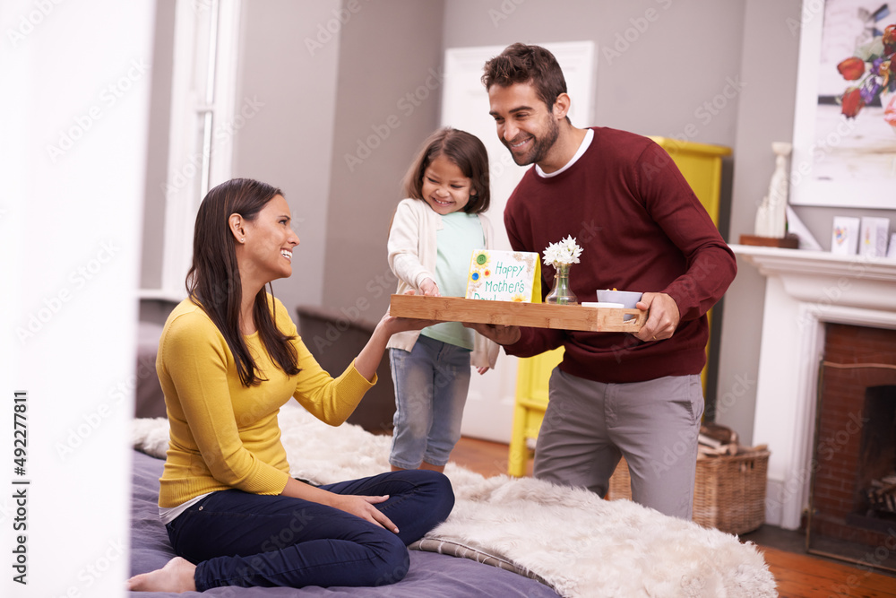 Spoiling mom. A man and his daughter bringing his wife breakfast in bed on Mothers day.