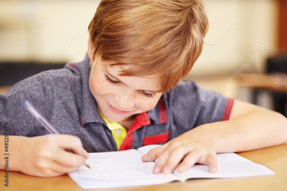 Happy to do his homework. A cute little boy doing his homework in class.