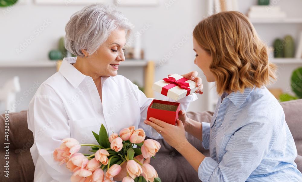 Young woman congratulations elderly mother with bouquet of fresh tulips