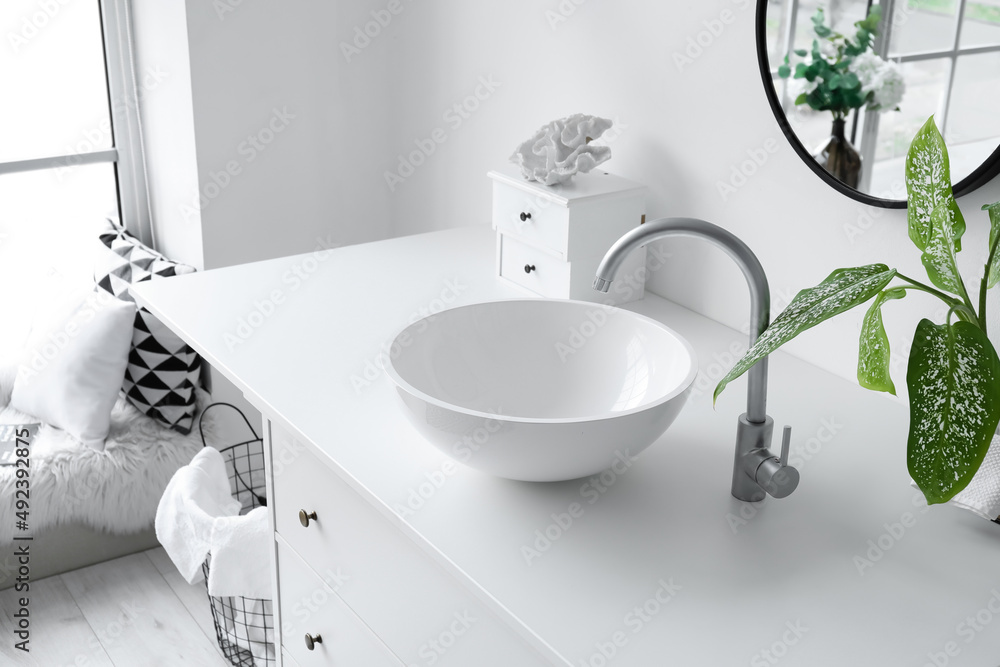 Modern sink with houseplant and drawers near light wall