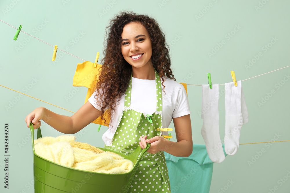 Young African-American woman with laundry basket and clothespins on color background