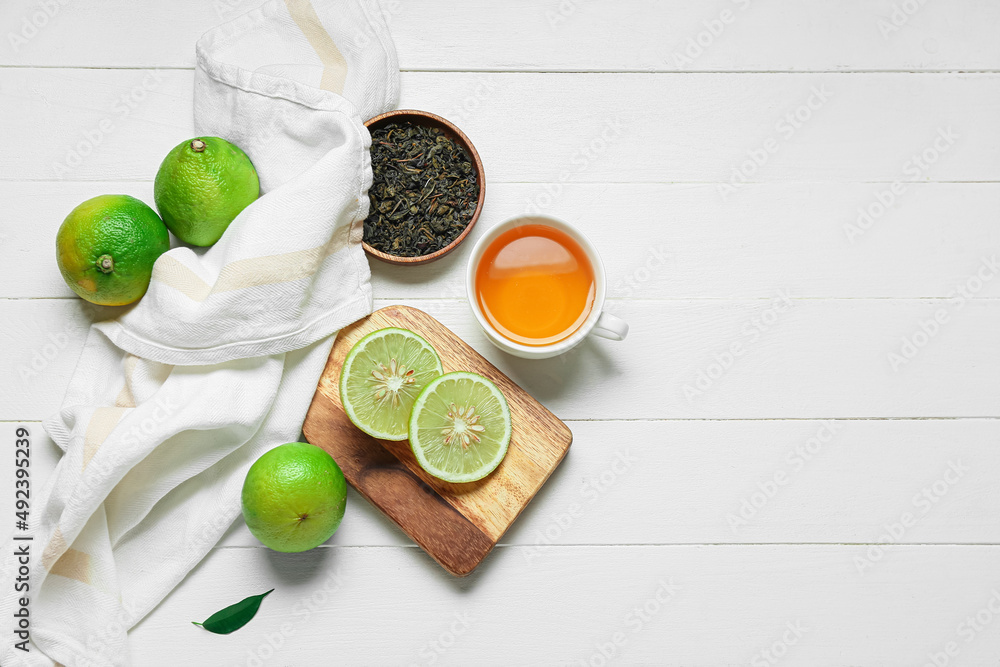 Composition with cup of tea, dried leaves and ripe bergamot fruits on white wooden background