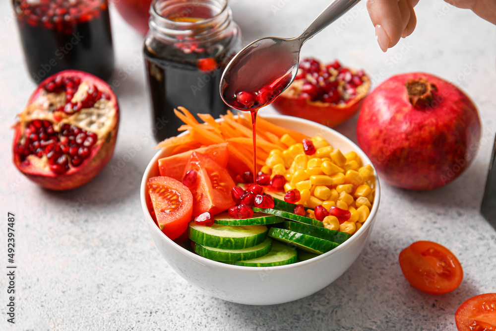 Pouring of pomegranate molasses onto fresh vegetable salad on light background