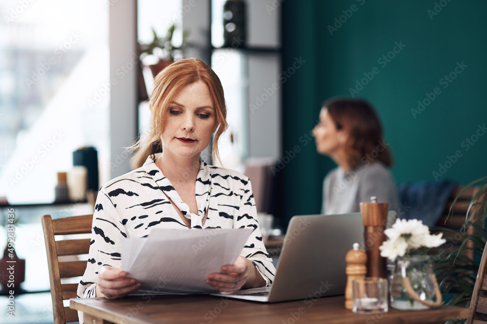 Everything looks in order. Cropped shot of an attractive middle aged woman doing paperwork while bei