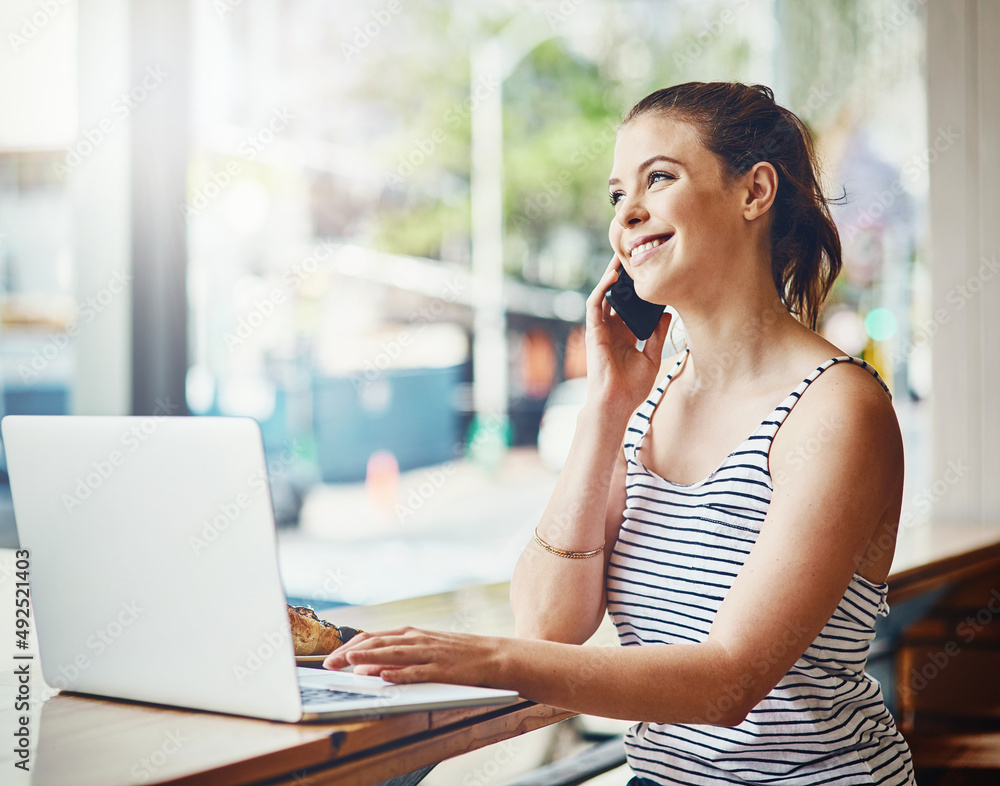 Staying productive in a relaxing atmosphere. Shot of a young woman talking on a cellphone and using 