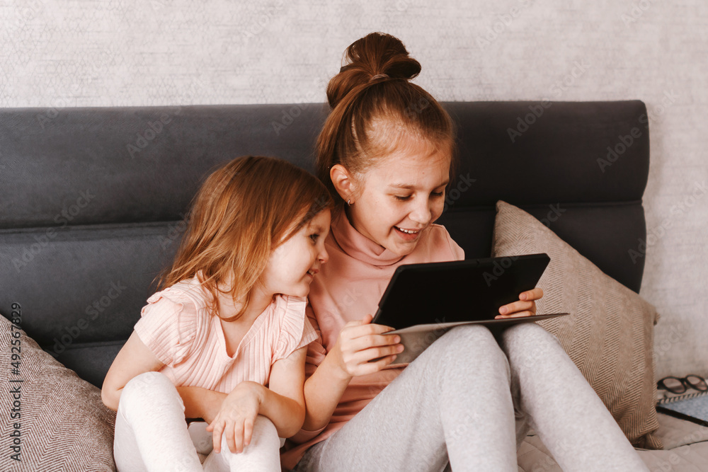 Two little girls sisters holding gadgets, spending time together