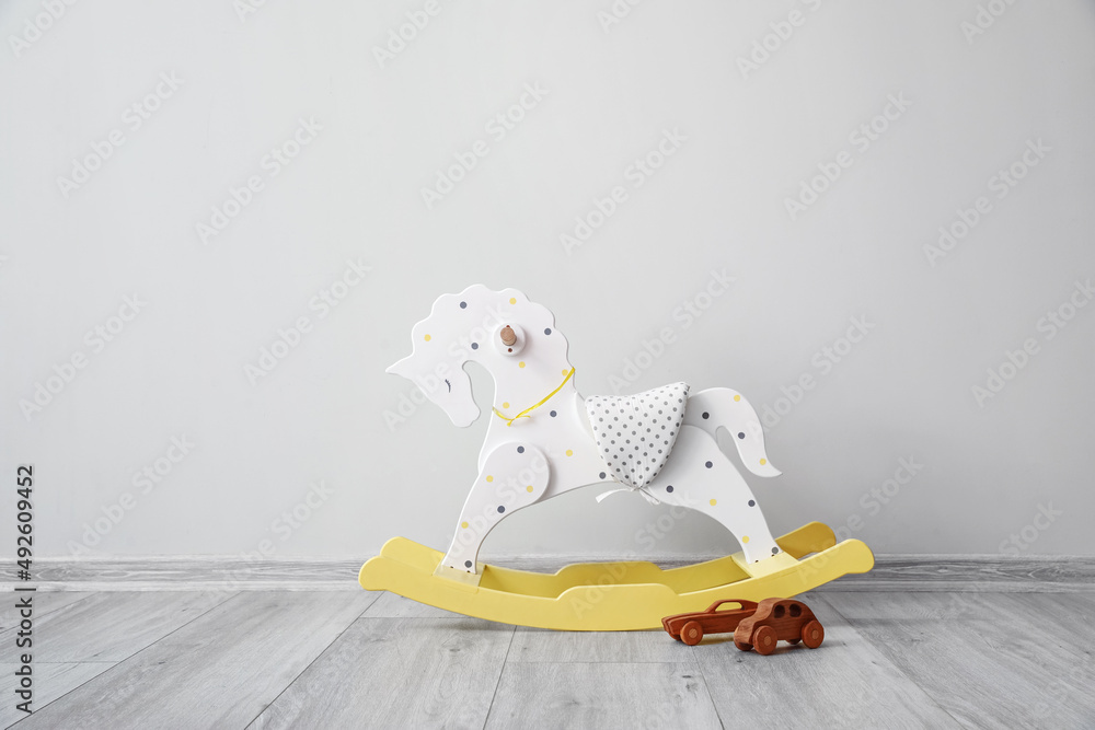 Rocking horse and wooden toy cars near light wall