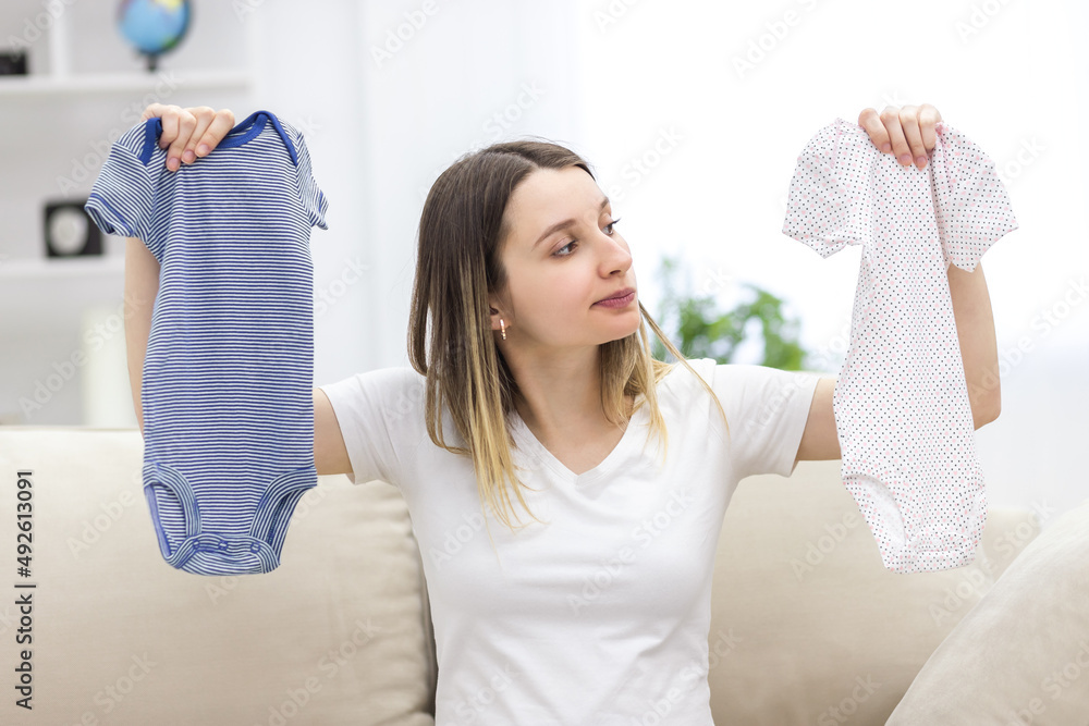 Photo of pregnant woman holding two child clothes.