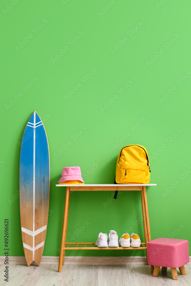 Desk with backpack, hat, shoes and surfboard near green wall in room