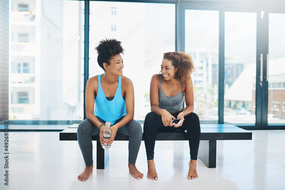 Lets take a bit of a breather. Portrait shot of two young fit women sitting down on a bench and havi