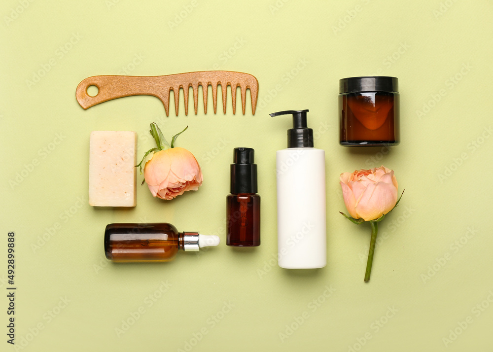 Composition with cosmetic products, hair comb and rose flowers on green background