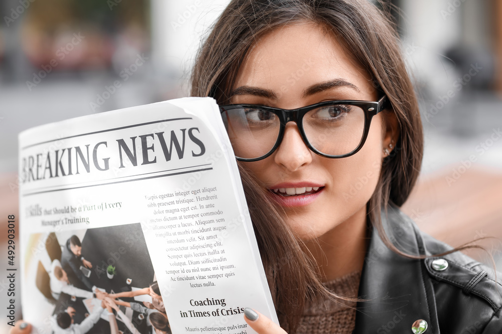 Young woman in eyeglasses with newspaper outdoors, closeup