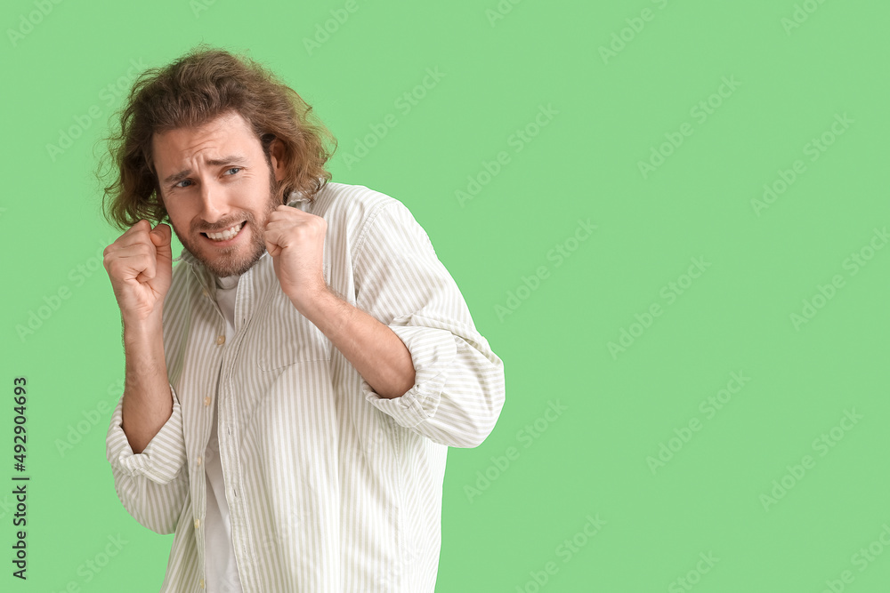 Scared young man in shirt on green background