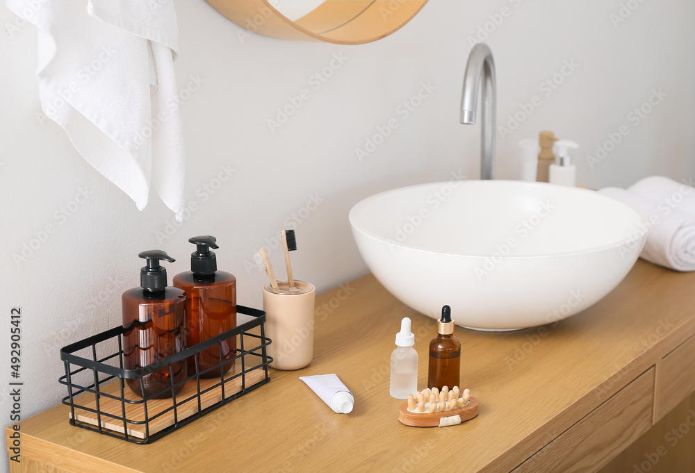 Toothbrushes, massage body brush and cosmetic products on table near white wall in bathroom