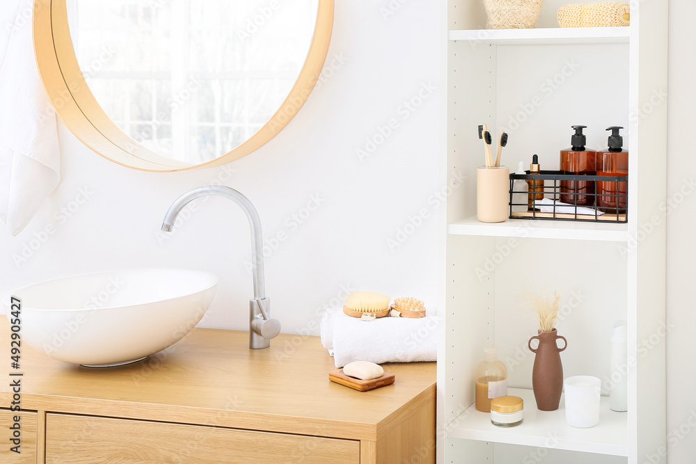 Shelf unit and table with different bath supplies near white wall in bathroom