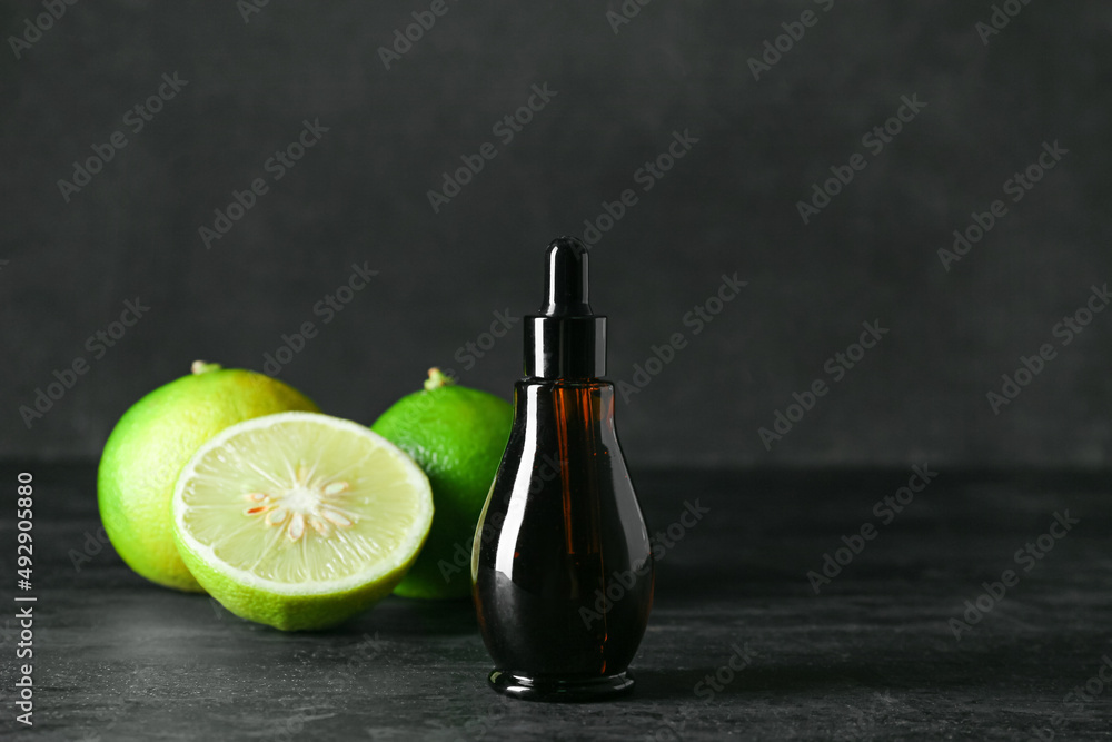 Bottle of essential oil and ripe bergamot fruits on dark background