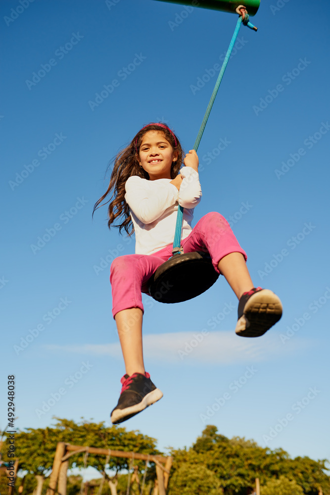 Check out my swinging skills. Portrait of a happy young girl playing on a swing at the park.