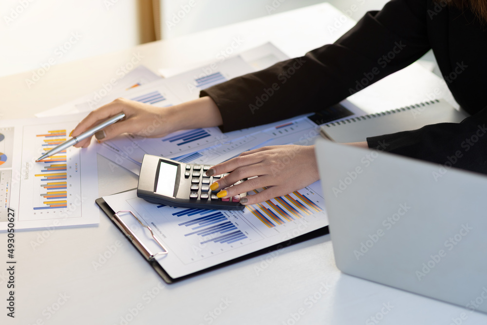 Businesswoman pointing at a business report chart and using a calculator for business analysis and a