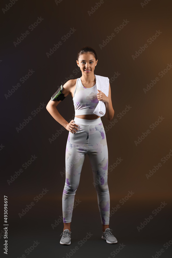 Sporty teenage girl with armband and towel on dark background