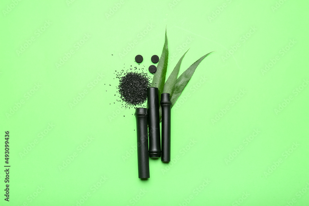 Composition with black bamboo sticks, activated carbon powder and pills on color background