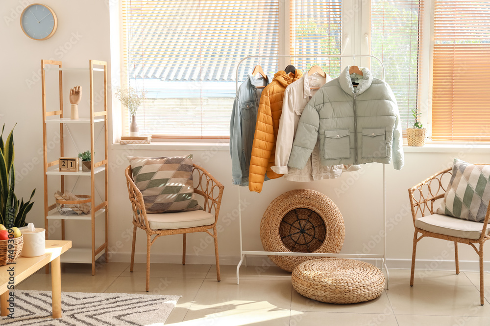 Interior of light room with armchair, shelving unit and warm jackets