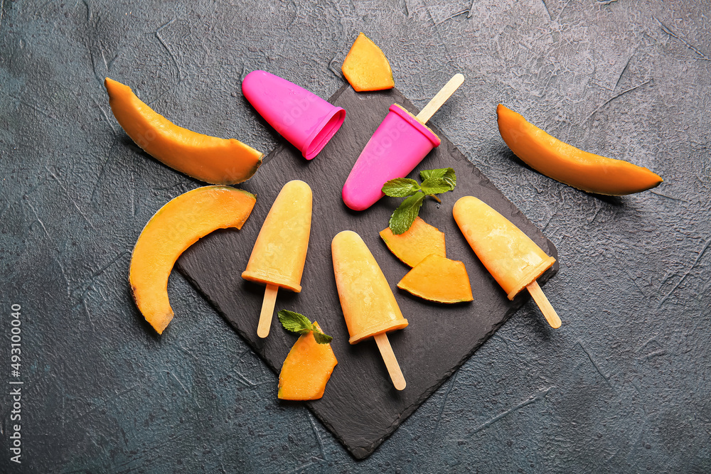 Board with tasty popsicles and melon pieces on dark background