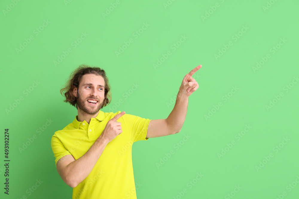 Handsome young man in stylish polo shirt pointing at something on green background