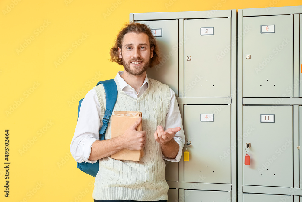 黄色背景储物柜附近有书的男学生