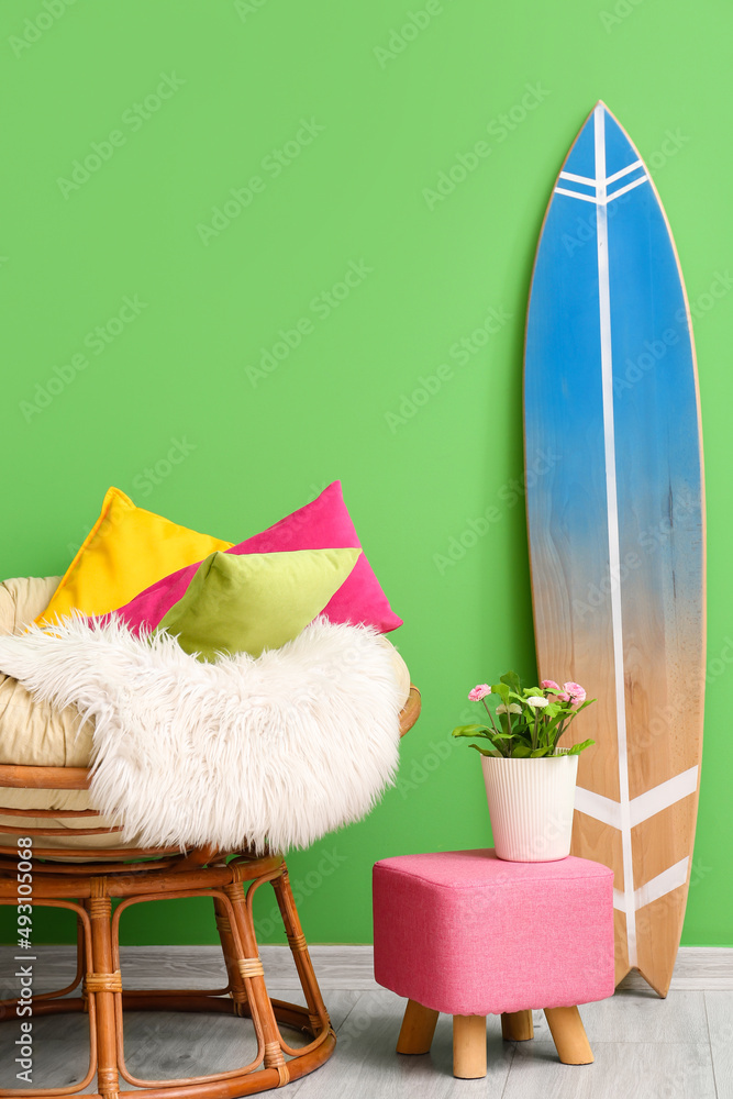 Comfortable armchair with soft pillows, pouf and surfboard near green wall in room