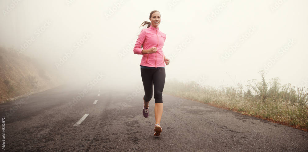 The miles are rolling away behind her. Shot of a young woman jogging on a country road on a misty mo