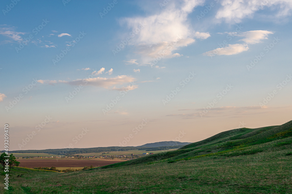 Green meadow with grass and hill and sky at sunset like in Scotland.