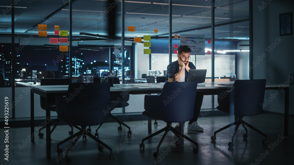 Successful Handsome Creative Director Working on Laptop Computer in Big City Office Late in the Even