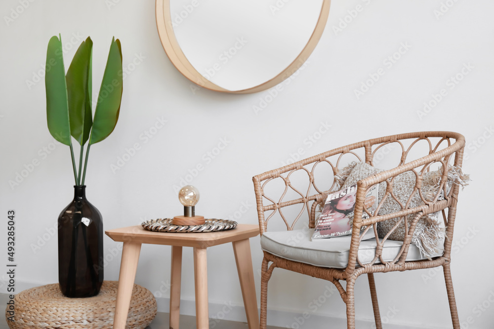 Vase with palm leaves, chair and table near light wall in room interior