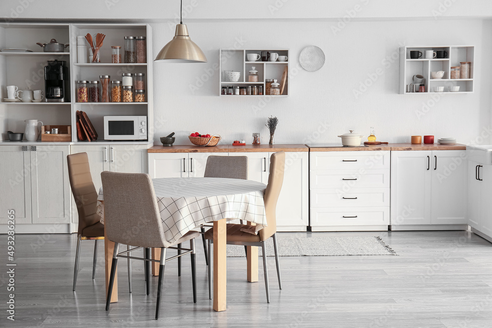 Interior of light modern kitchen with white counters, dining table and shelves