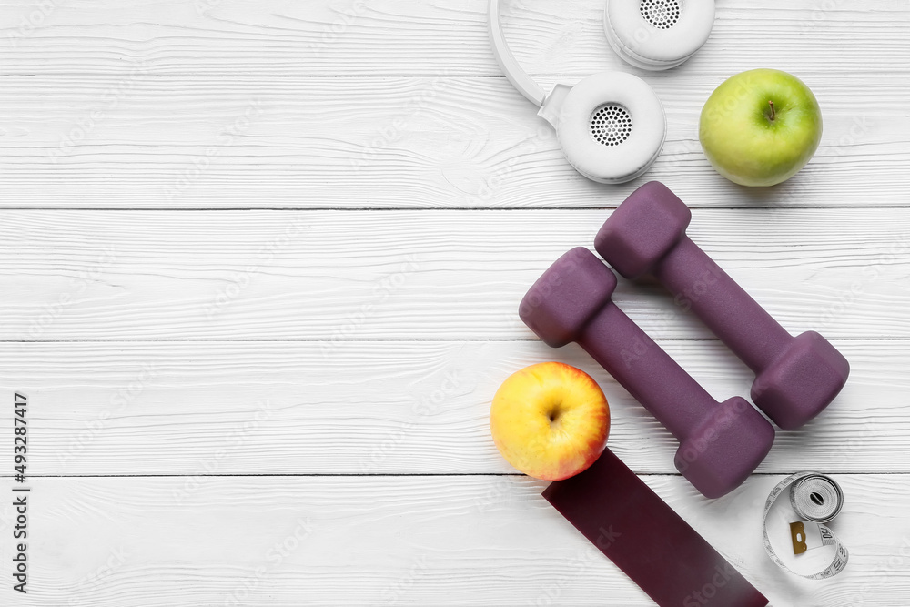 Stylish sport equipment, apples and headphones on light wooden background