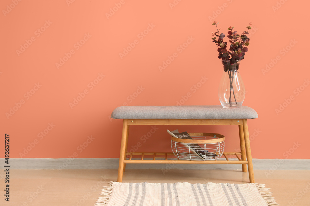 Soft bench with eucalyptus in vase, basket and magazine near pink wall