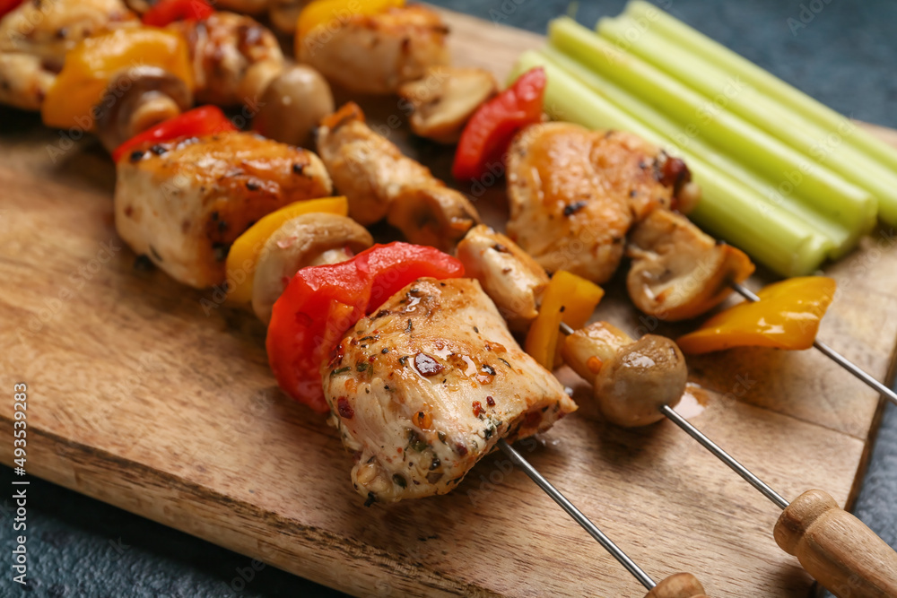 Wooden board of grilled chicken skewers with vegetables on table, closeup