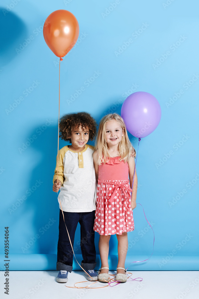 Shes my childhood sweetheart. Portrait of a cute little girl and boy holding a balloon over a blue b