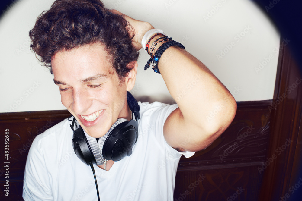 Trendy young DJ. Shot of a stylish young man wearing headphones around his neck and running his hand