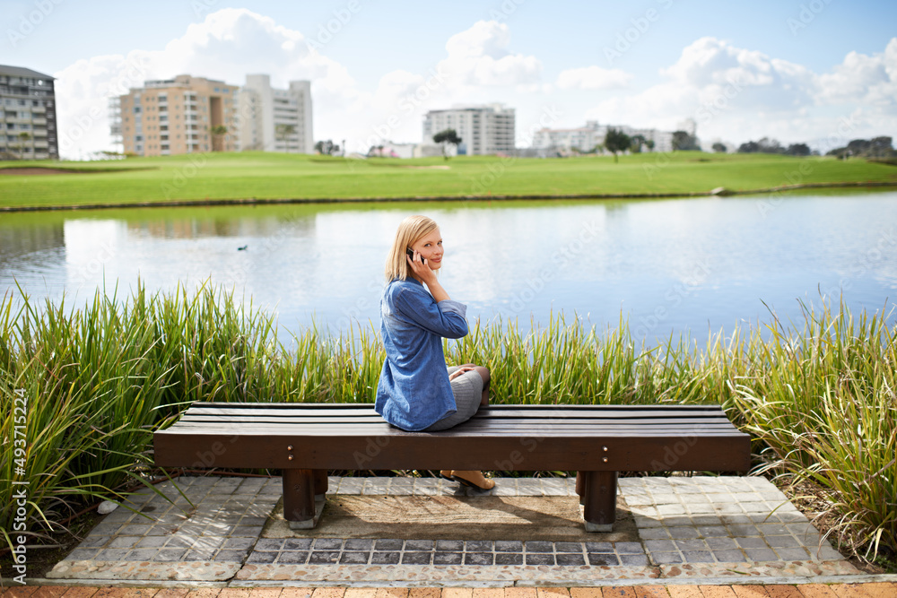 Away from the hustle and bustle. Rear view shot of a blonde woman talking on her phone on the park b